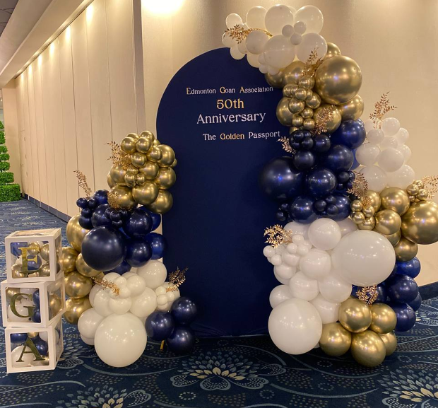 “A decorative photo zone with white, gold and dark blue balloons for a 50th anniversary celebration, against a blue arch with inscriptions.”
