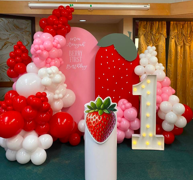 Children's photo zone with red, pink and white balloons, a large strawberry and a light-up number 1 for a first birthday